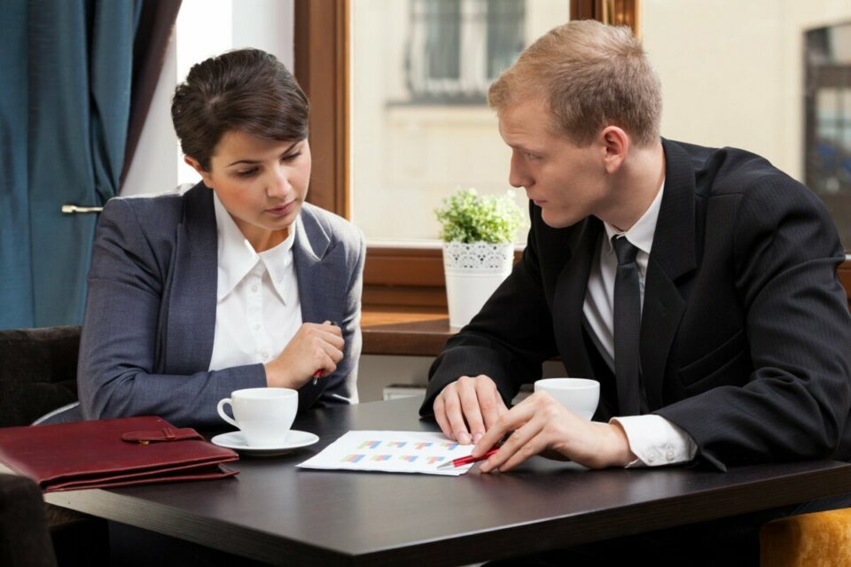 man and a woman in their business attires having a meeting while drinking coffee